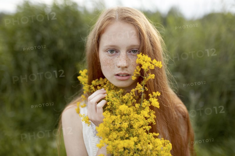 Portrait of serious Caucasian girl with freckles holding wildflowers