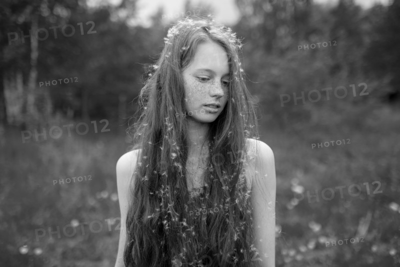 Caucasian girl standing in field with fuzz in hair