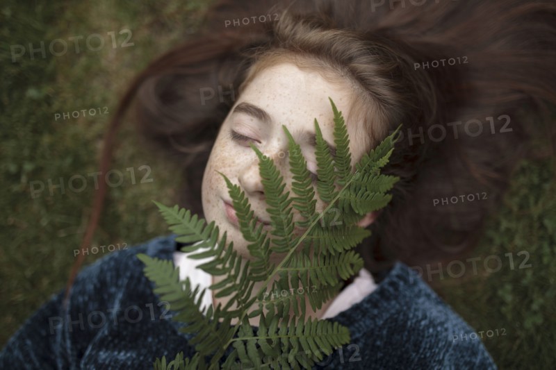 Caucasian girl laying in grass holding branch