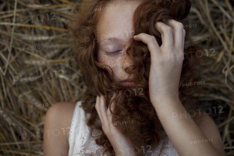 Caucasian girl laying in wheat holding hair