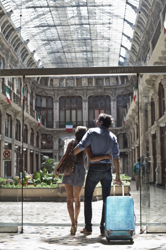 Caucasian couple pulling luggage into ornate building