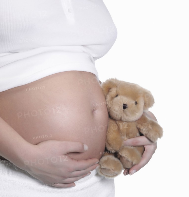 Caucasian woman holding teddy bear to pregnant belly