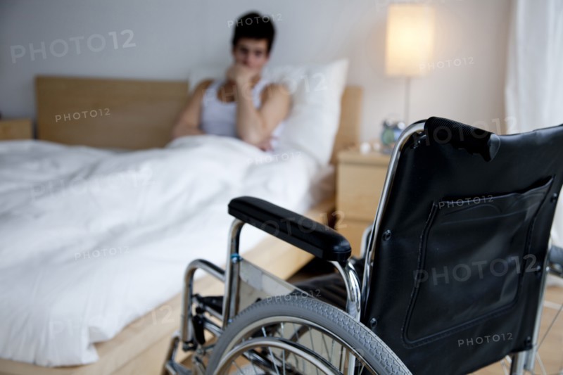 Disabled Caucasian man in bed out of reach of wheelchair