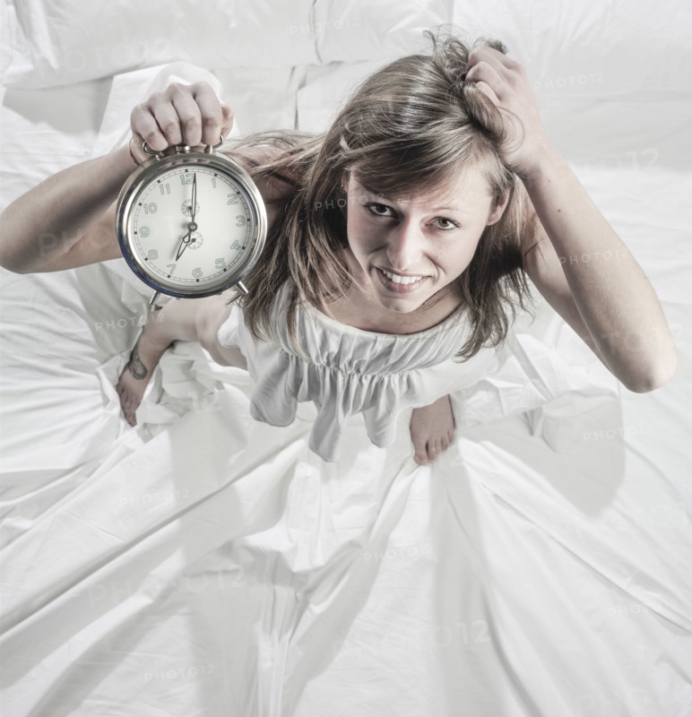 Hispanic woman holding alarm clock in bed