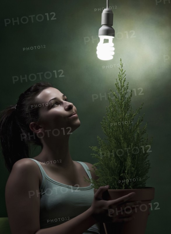 Caucasian woman holding potted plant under cfl lightbulb
