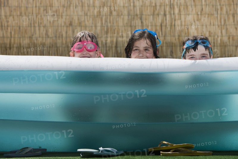 Smiling Caucasian children hiding in inflatable swimming pool