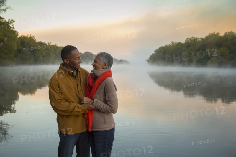Older couple hugging at foggy river at sunrise