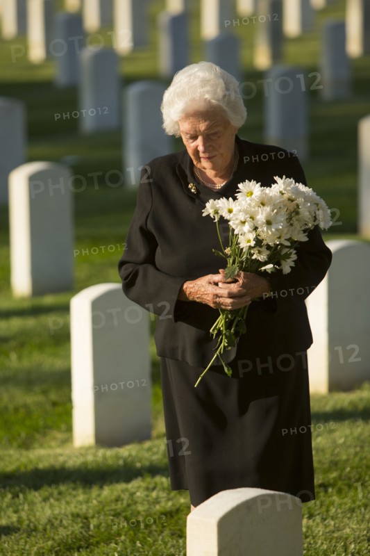 Caucasian widow holding bouquet at cemetery gravestone