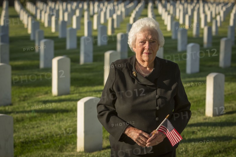 Caucasian widow holding American flag in cemetery