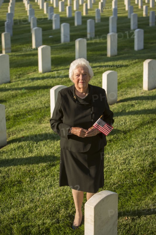 Caucasian widow holding American flag in cemetery