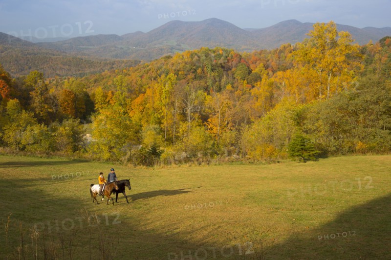 Distant Caucasian couple horseback riding in field