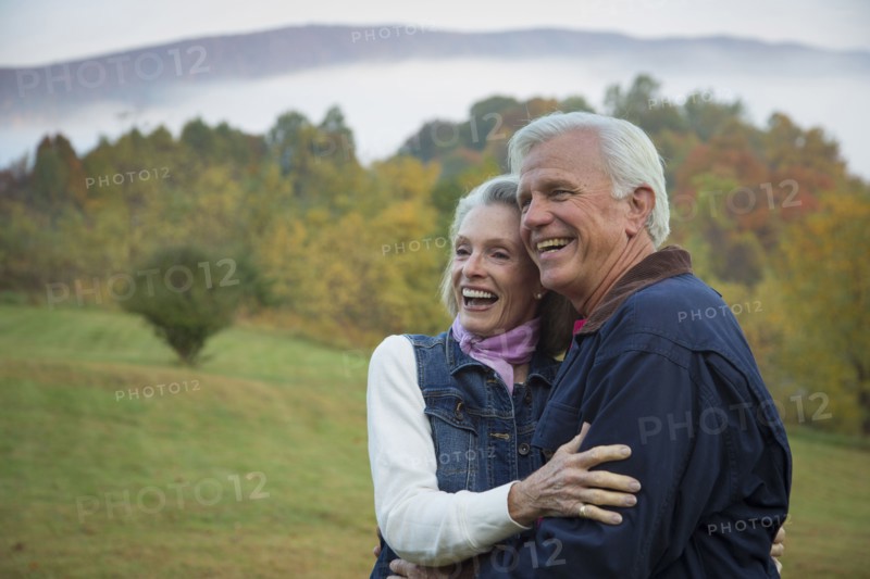 Older Caucasian couple hugging in field