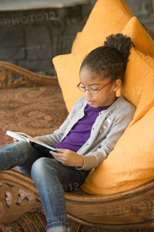 Mixed Race girl sitting on sofa reading book