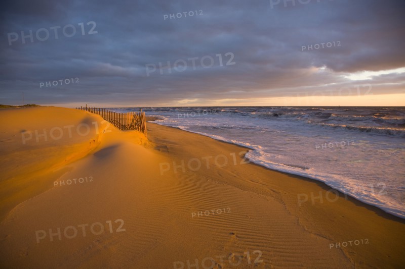 Ocean waves near sand dunes at sunset