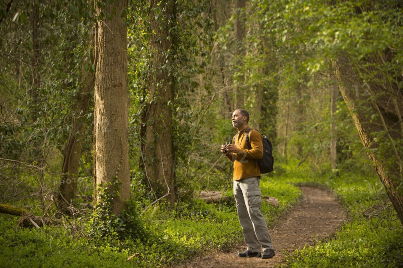 African American man standing on path in forest holding binoculars
