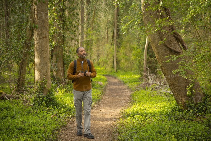 African American man walking on path in forest holding binoculars