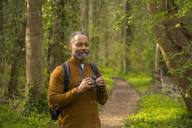 African American man standing on path in forest holding binoculars