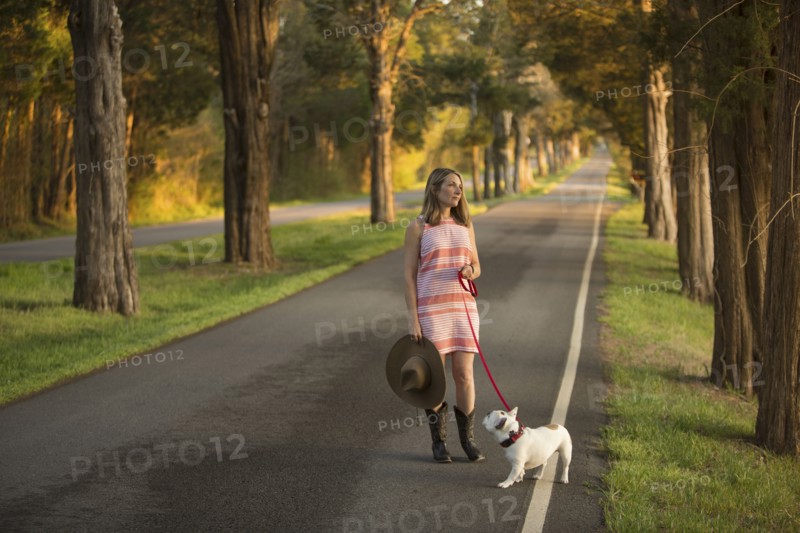 Caucasian woman holding a cowboy hat walking dog