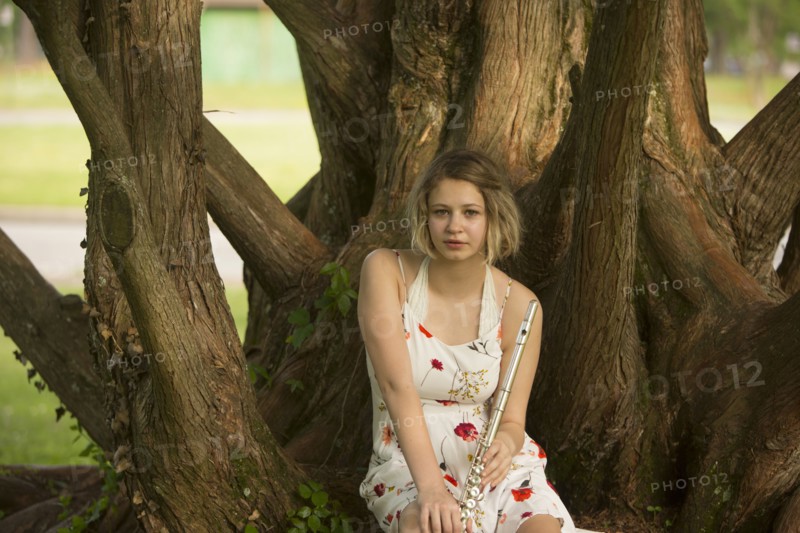 Caucasian teenage girl sitting on tree root holding flute