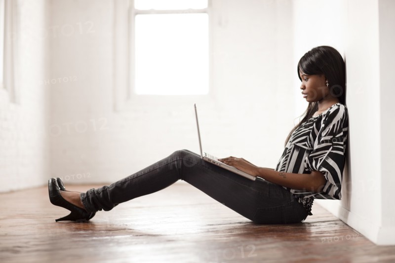 African woman using laptop on floor of empty room