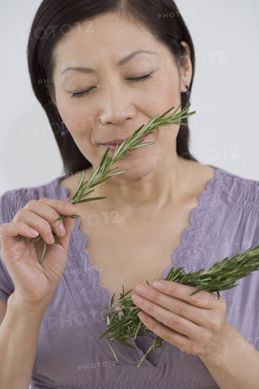 Middle-aged Asian woman with eyes closed smelling springs of rosemary