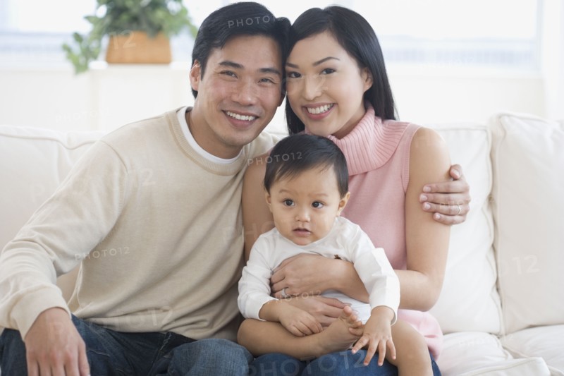 Asian parents holding baby on sofa