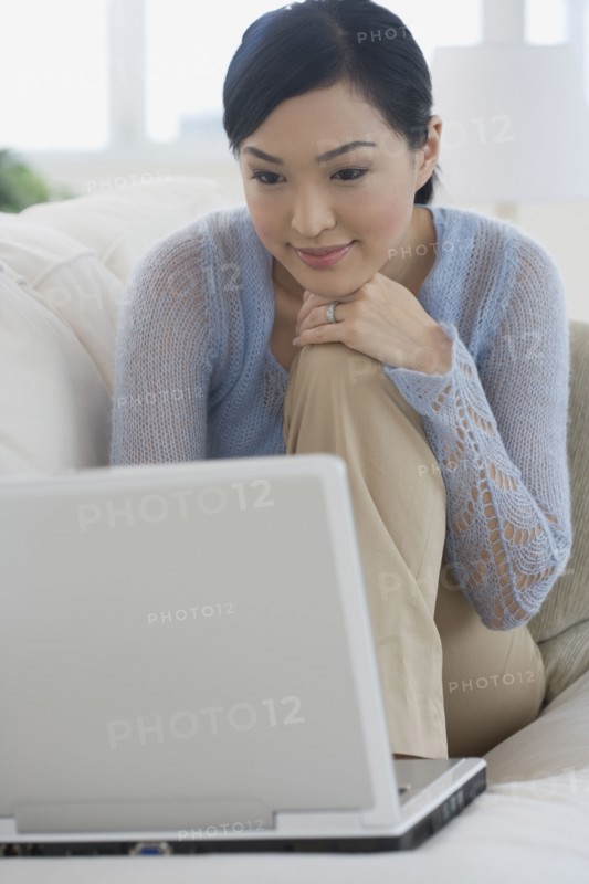Asian woman using laptop on sofa