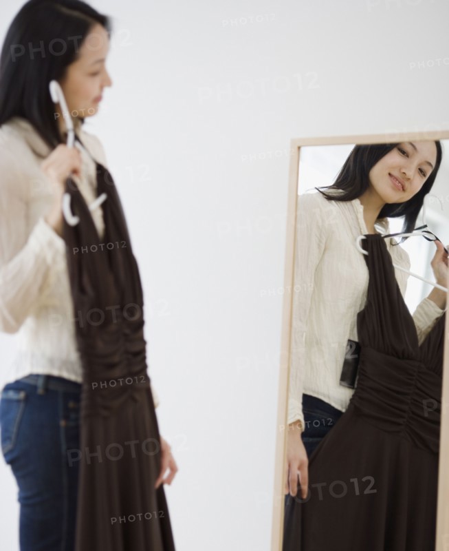 Asian woman holding dress up in front of mirror