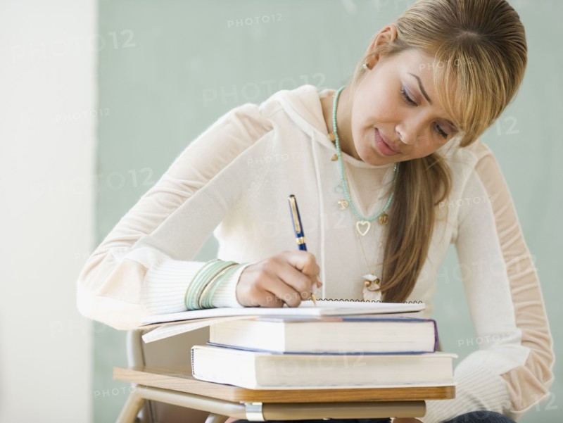 Young Hispanic woman writing at school desk