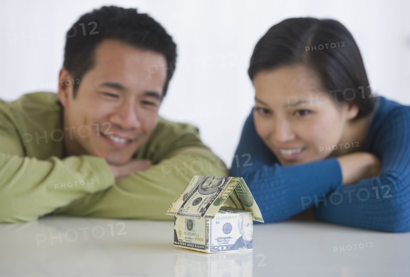 Asian couple looking at house made of money