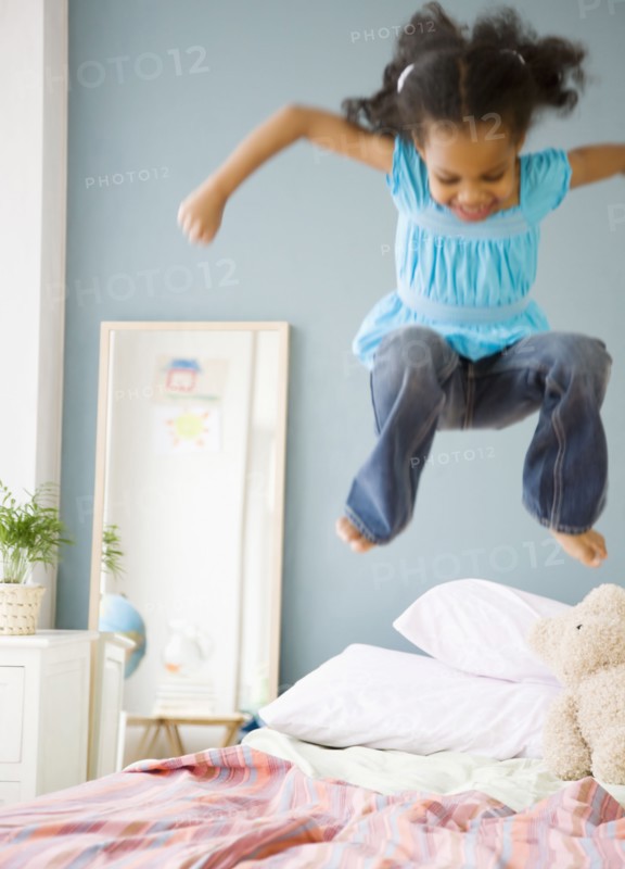 Mixed race girl jumping on bed