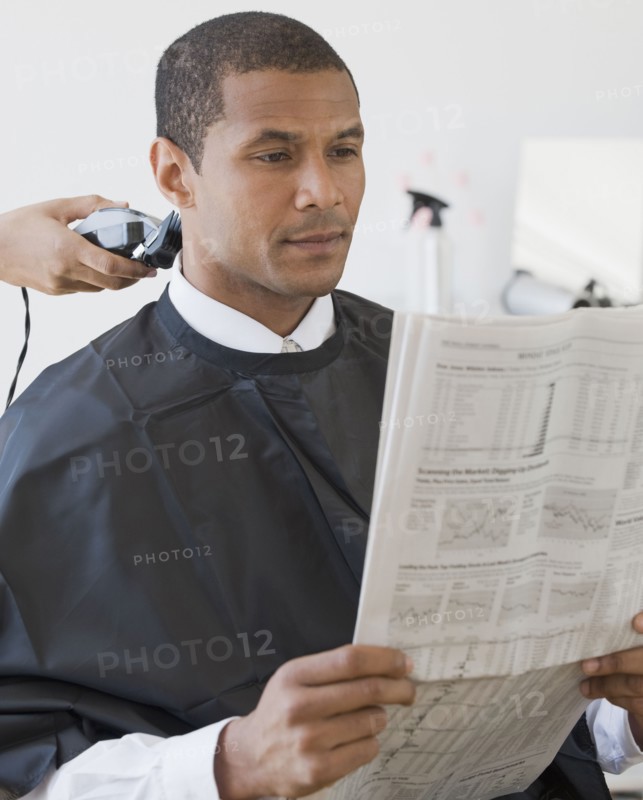African man reading paper at barbershop