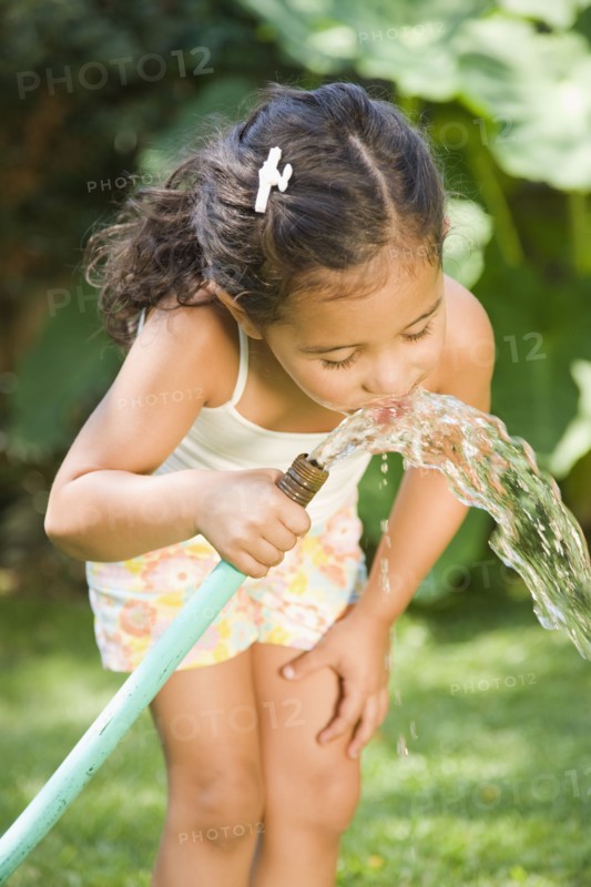Hispanic girl drinking from hose