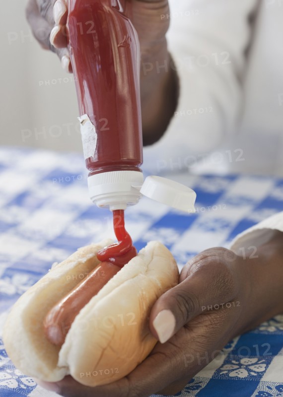 African woman putting ketchup on hot dog