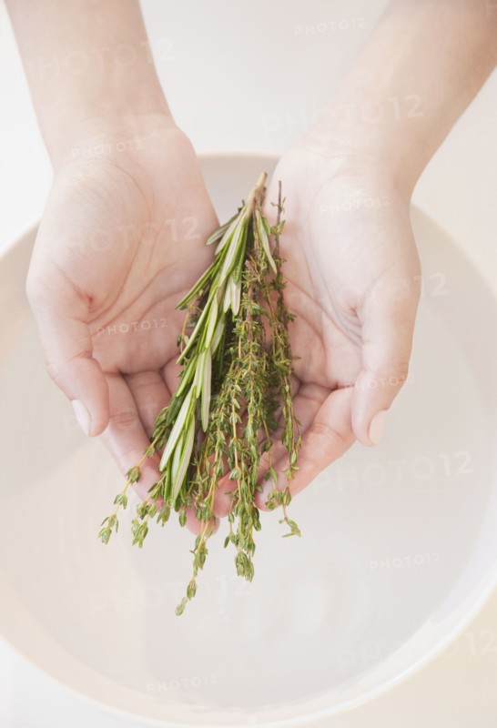 Woman holding fresh herbs over bowl of water