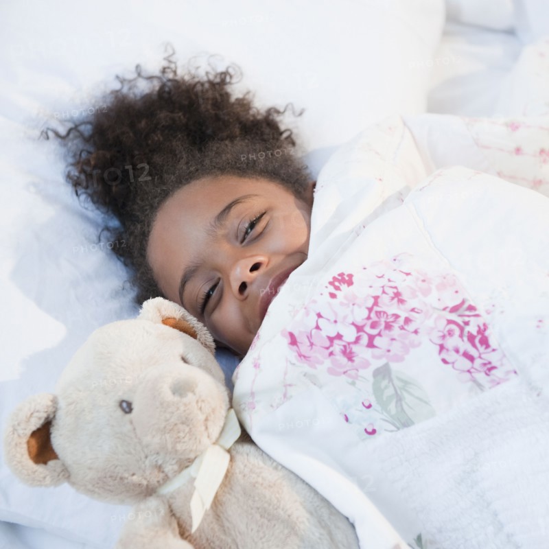 Mixed race girl in bed with teddy bear