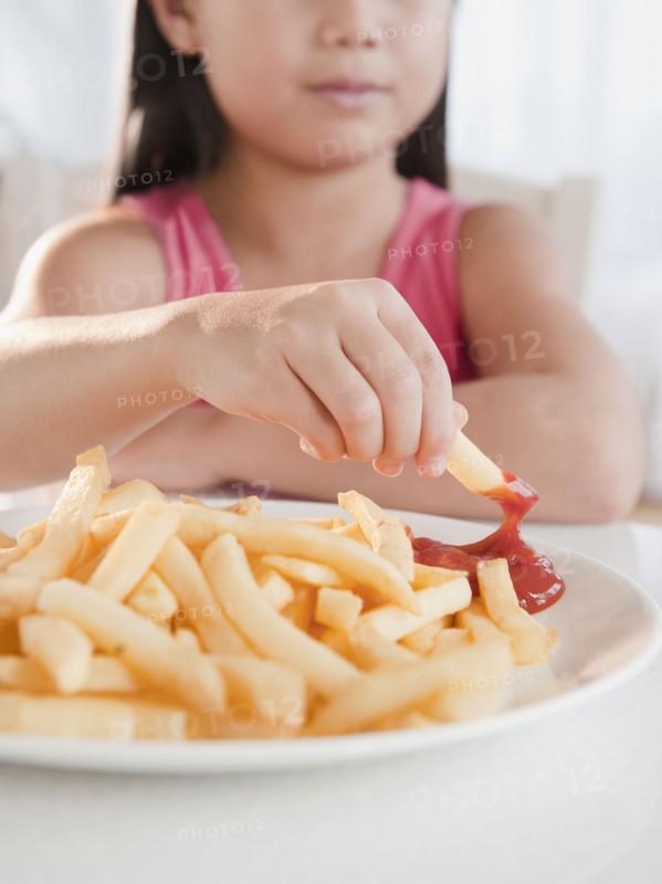 Mixed race girl eating French fries and ketchup