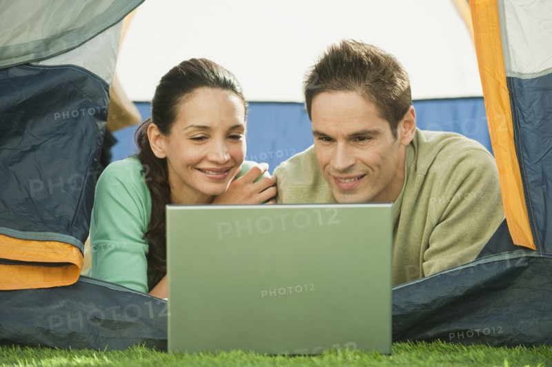 Hispanic couple using laptop in tent
