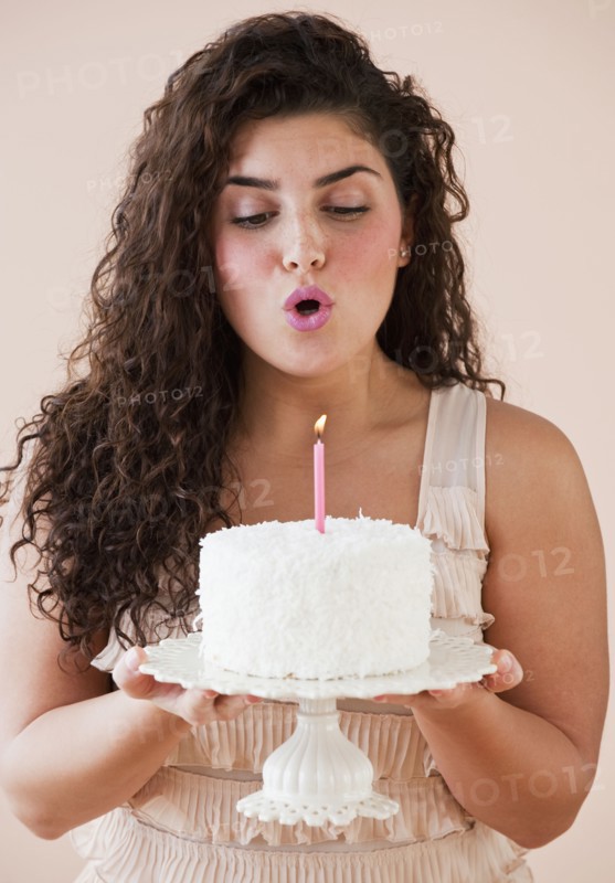 Mixed race woman blowing out candle on birthday cake