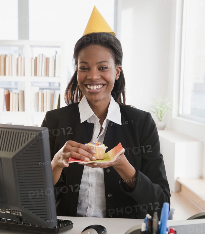 Mixed race businesswoman eating birthday cupcake