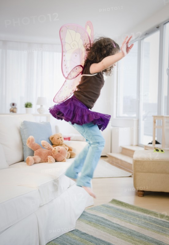 Hispanic girl in fairy wings jumping off couch