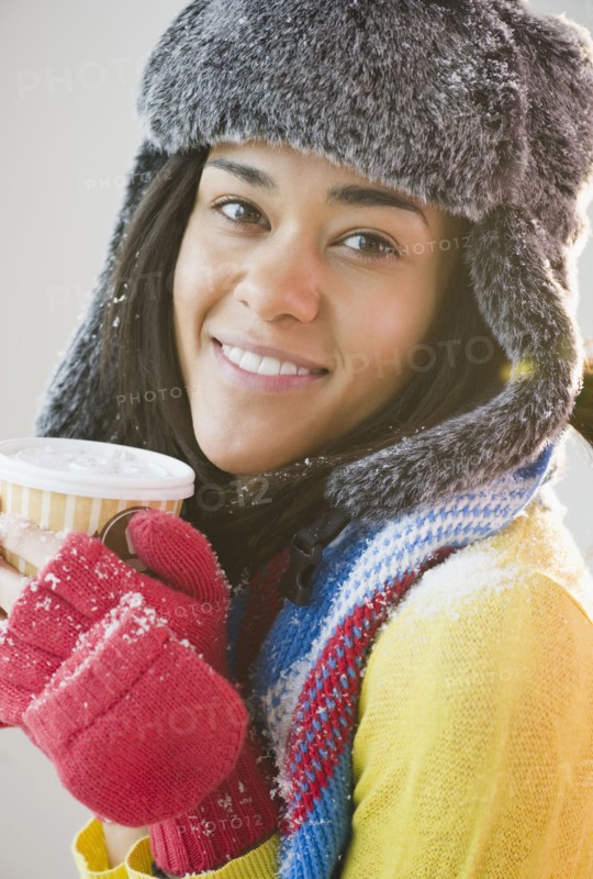 Mixed race woman in hat and gloves drinking coffee