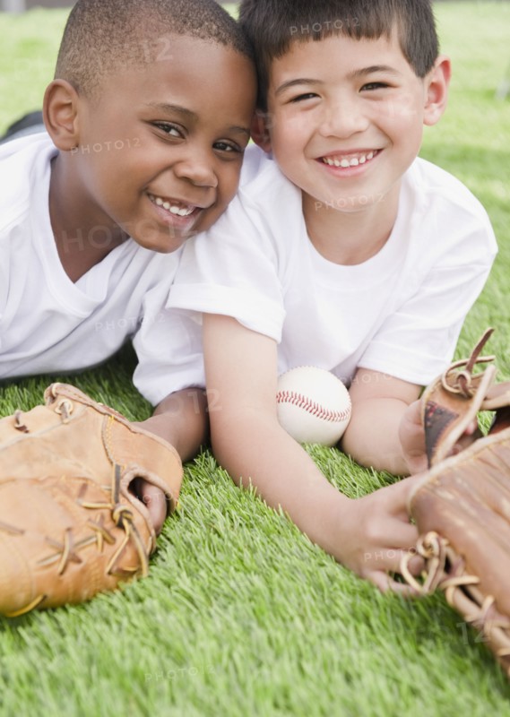 Boys laying in grass with baseball and baseball gloves