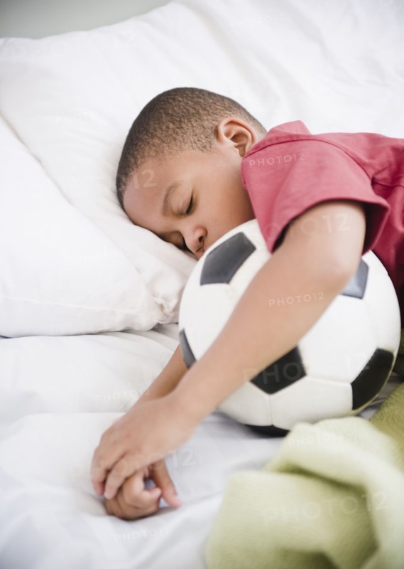 African American boy sleeping with soccer ball