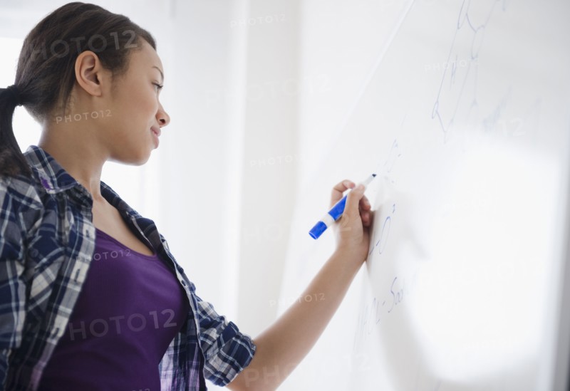 Mixed race teenage girl writing on whiteboard in classroom