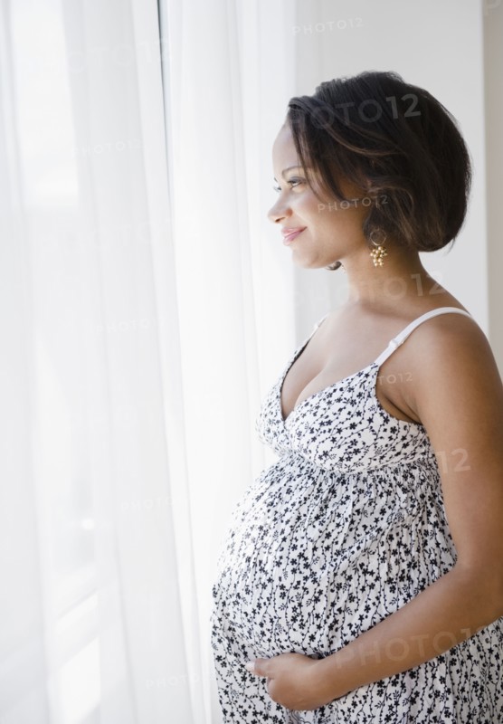 Smiling pregnant Black woman looking out window