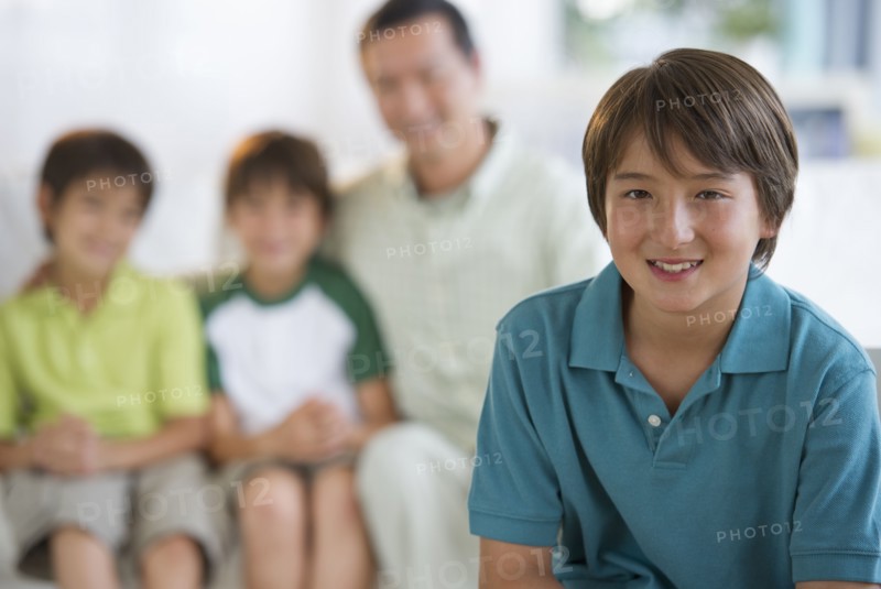 Smiling boy in living room with father and brothers in background