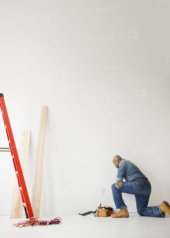 African American construction worker kneeling to look at wall