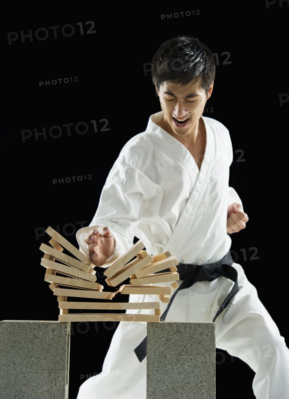 Asian male karate black belt breaking wooden planks