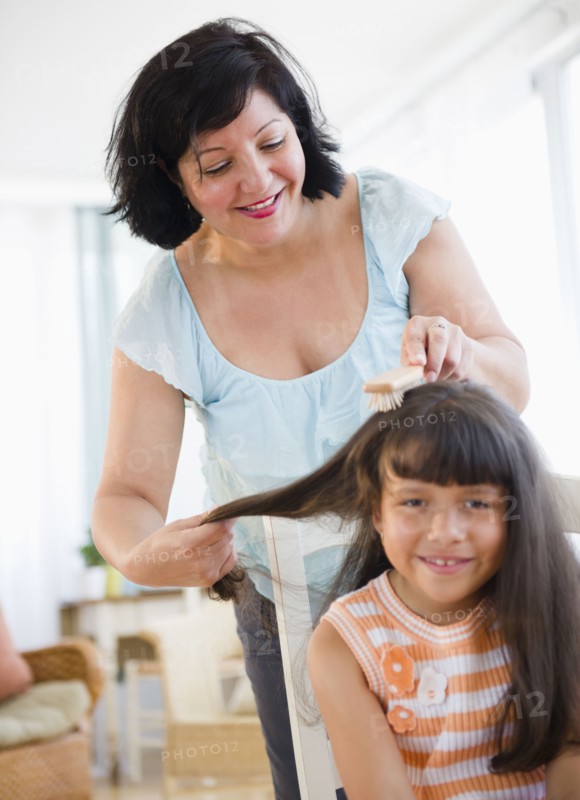 Hispanic woman brushing daughter's hair